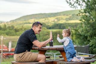 An image of a dad and his daughter having fun, leaning in to high-five on a picnic bench.