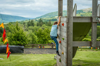 An image of a boy using a climbing wall, with a backdrop of countryside greenery.