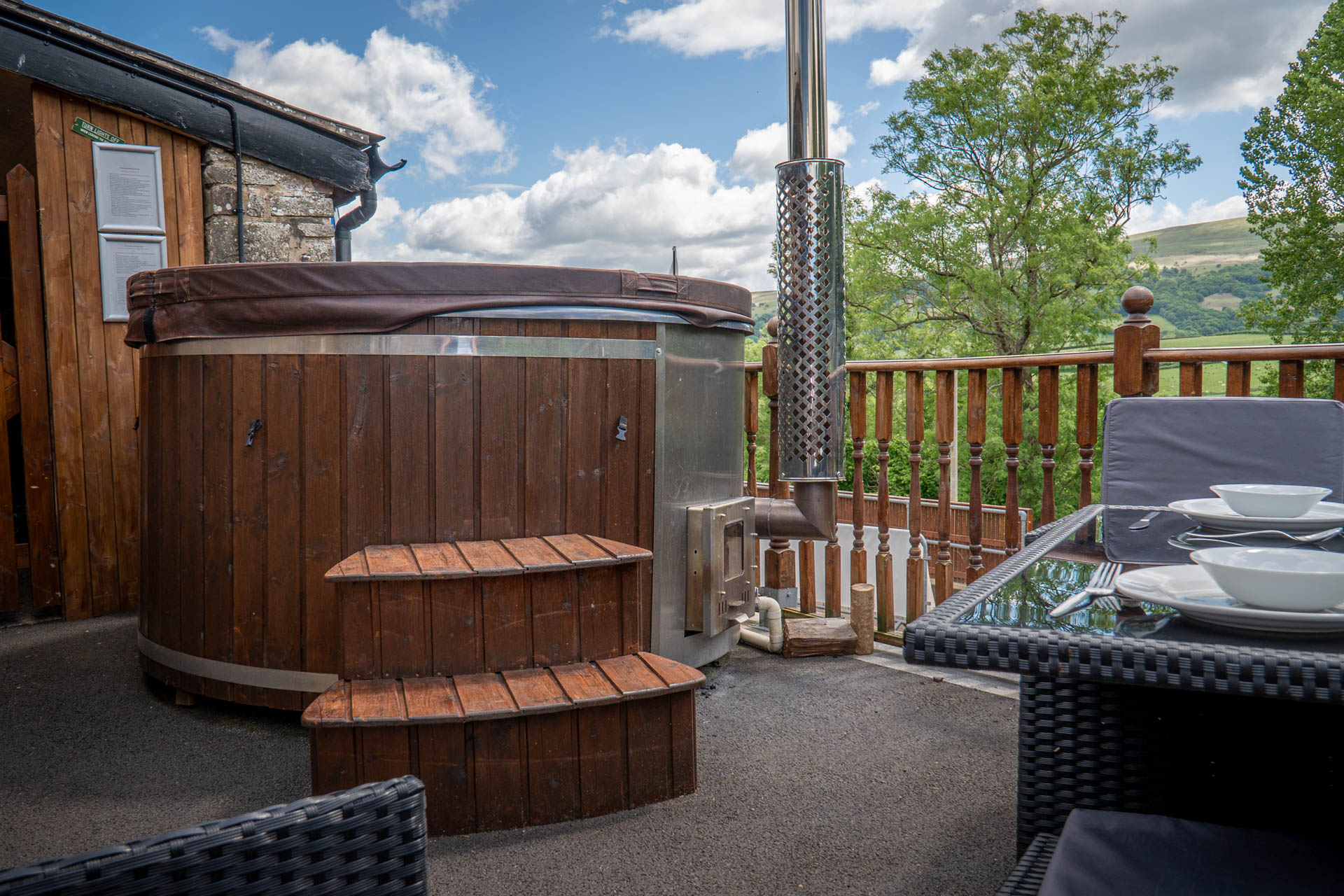 An image of The Milking Parlour's wood fired hot tub and outdoor seating, with a stunning view of the Brecon Beacons.