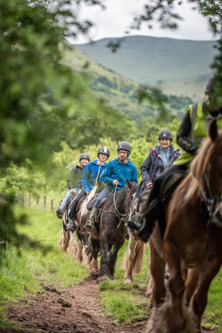 An image of riders on horseback returning from their Brecon ride, down a dirt track.