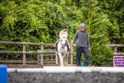 An image of a girl riding a white pony around Cantref Riding Centre's training area, the pony is being led round by the girl's mum.