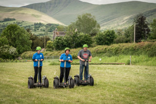 An image of a group of three using Segways on the grass practice field, with a striking view of the Brecon Beacons.