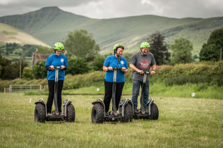 An image of a group of three using Segways on the grass practice field, with a striking view of the Brecon Beacons.