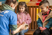 An image of a girl with a guinea pig rested on her lap. Whilst she gently strokes the guinea pig, a boy waits patiently for his turn.