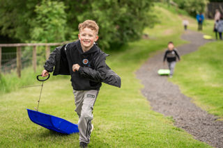 An image of a young boy smiling from ear to ear as he returns from the bottom of the super sledge ride at Cantref Adventure Farm.