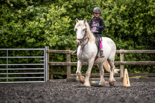 An image of a girl riding a small white horse around Cantref Riding Centre's training area.