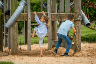 An image of a girl climbing a wooden ladder and a boy getting ready to shovel sand.