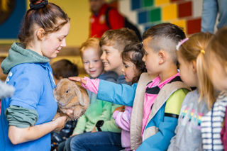 An image of children lined up to stroke a bunny, which is being held by a member of the Cantref team.